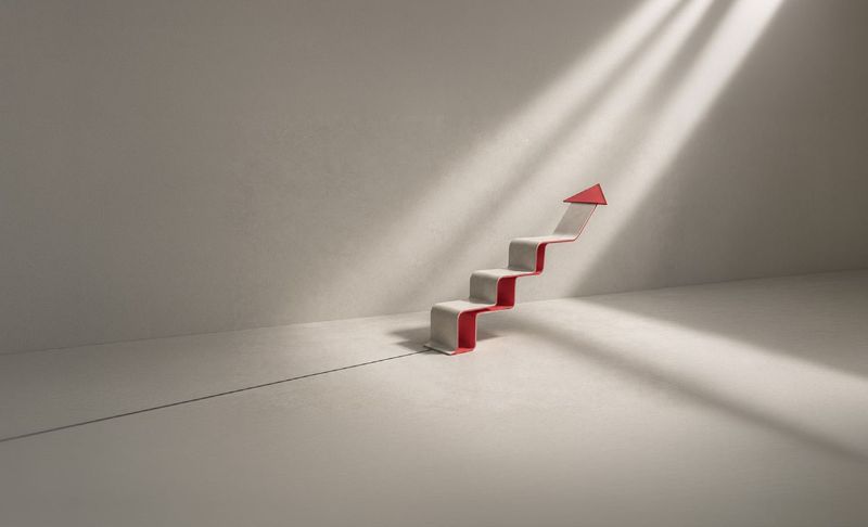 Escada em forma de seta vermelha subindo em um ambiente de concreto iluminado por feixes de luz