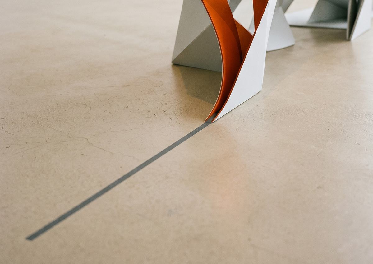Fita de papel laranja saindo de uma escultura branca sobre piso de concreto claro